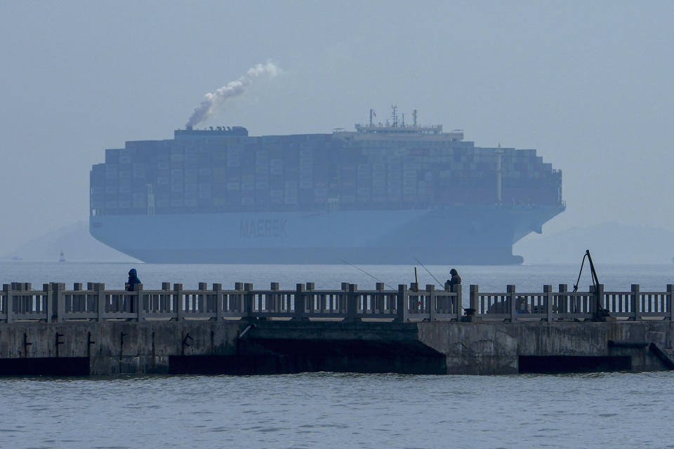 People fish as a containers vessel sails by a port shrouded by haze in Xiamen in southeast China's Fujian province on Dec. 27, 2023. The United Nations issued a somber global economic forecast for 2024 on Thursday, Jan. 4, 2024 pointing to challenges from escalating conflicts, sluggish global trade, persistently high interest rates and increasing climate disasters. (AP Photo/Andy Wong)