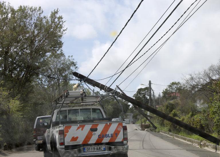 Motorists drive past damaged utiliy poles in the aftermath of the hurricane Gonzola on October 14, 204 on the French Caribbean island of Saint Martin