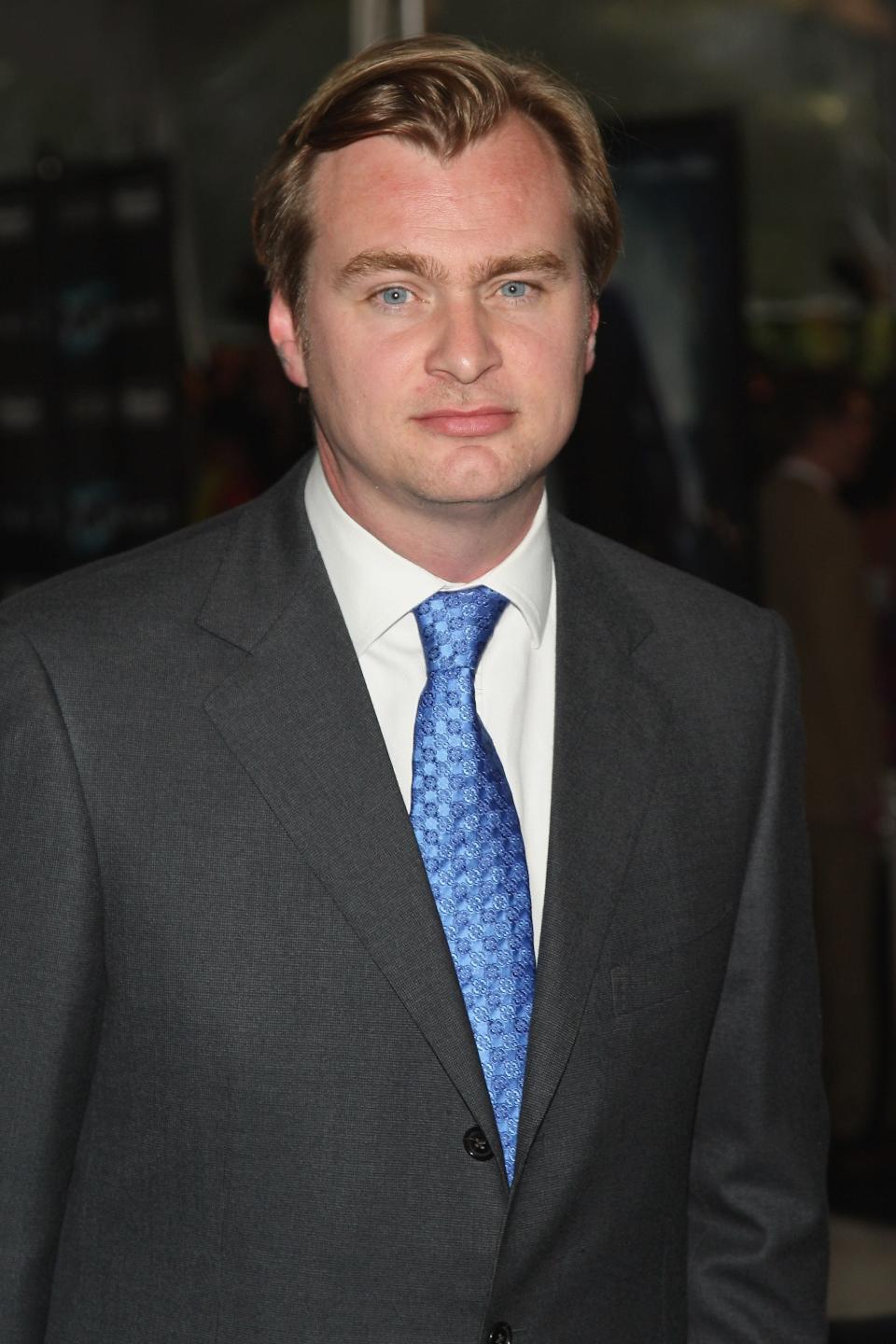 Christopher Nolan in a grey suit and blue tie