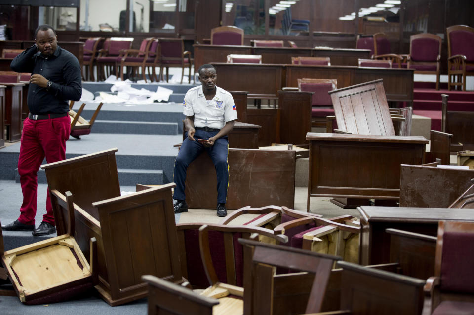 FILE - In this Sept. 3, 2019 file photo, a security officer sits amid overturned tables inside Parliament after it was vandalized in Port-au-Prince, Haiti. Opposition lawmakers turned desks over in the Chamber of Deputies, hours before the planned ratification of Prime Minister Fritz William Michel. The vote was indefinitely postponed. (AP Photo/Dieu Nalio Chery, File)