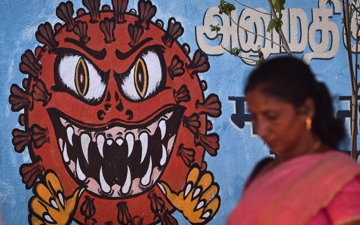 Woman walks past a scary mural of the Covid-19 particle - Idrees Mohammed/Shutterstock