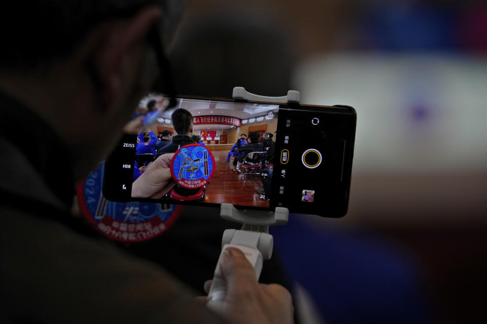 An attendee films a badge depicting the Tiangong space station as Chinese astronauts for the upcoming Shenzhou-18 mission Li Guangsu, Ye Guangfu and Li Cong meet with media members at the Jiuquan Satellite Launch Center in northwest China, Wednesday, April 24, 2024. (AP Photo/Andy Wong)