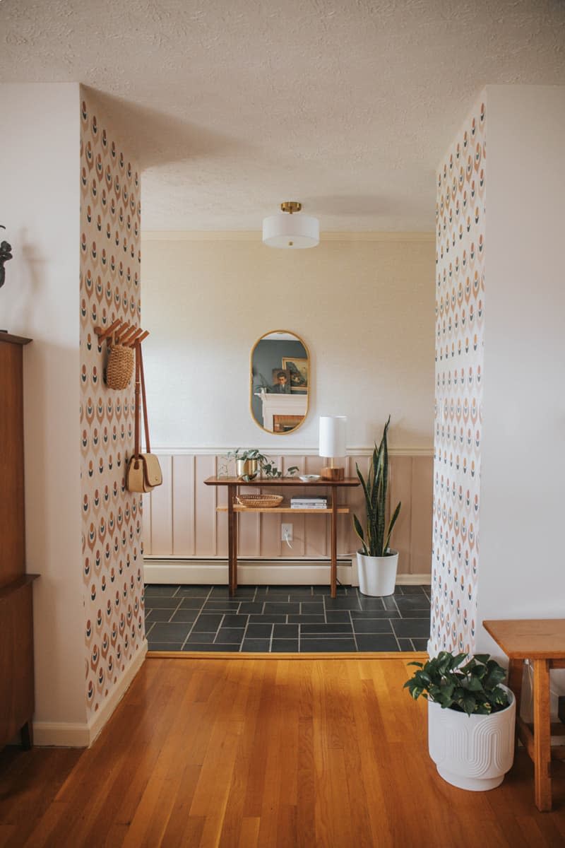 wood floors, hallway, black ceramic tile floor, wallpaper on accent walls, round vintage lighting fixture, small entry table