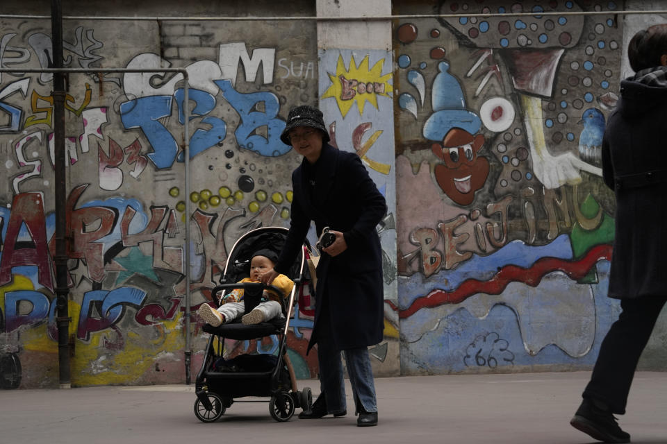 A woman pushes a child in a pram near graffiti art at a trendy district popular with youths in Chengdu, the capital of the southwestern China's Sichuan province, Sunday, March 17, 2024. Sichuan has come to dominate in the industry as rap has gone mainstream, with the region's dialect lending itself to rhymes and some of the biggest acts coming from the region. (AP Photo/Ng Han Guan)