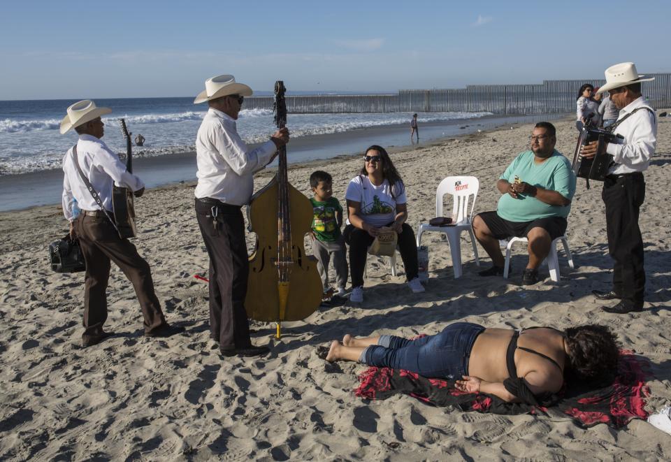 Musicians talk to tourists after performing at the Mexican side of the border with the U.S. at the Pacific Ocean, Tijuana, Mexico, Friday, Nov. 16, 2018. With about 3,000 Central American migrants having reached the Mexican border across from California and thousands more anticipated, the mayor of Tijuana said Friday that the city was preparing for an influx that will last at least six months and may have no end in sight. (AP Photo/Rodrigo Abd)