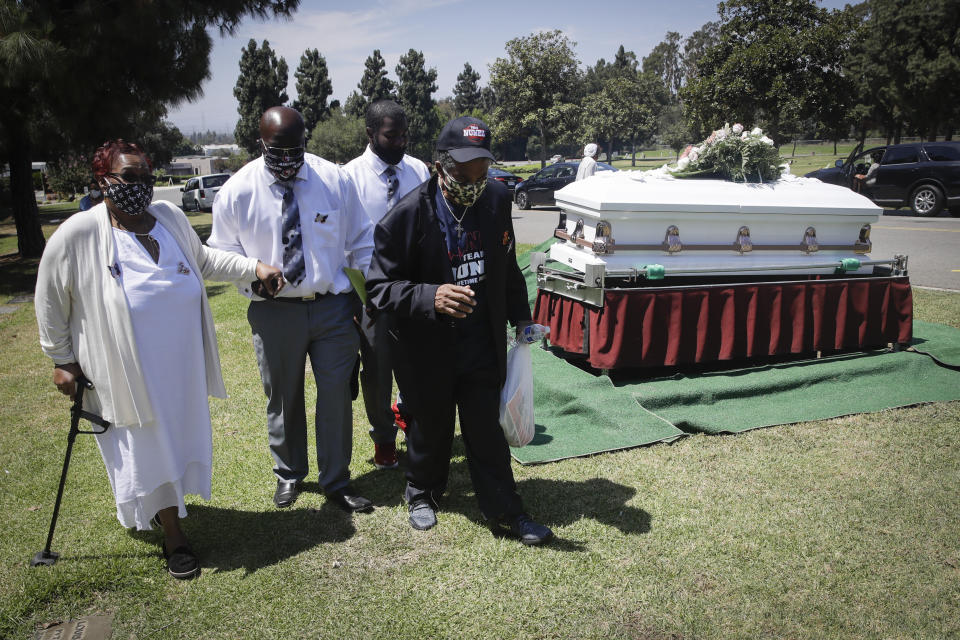 Relatives of Lydia Nunez, who died from COVID-19, her mother Lorraine, left, brother-in-law Jesse Banks, second from left, and gather Samuel, at right, walk past her casket during her burial at the Rose Hills Memorial Park Tuesday, July 21, 2020, in Whittier, Calif. (AP Photo/Marcio Jose Sanchez)