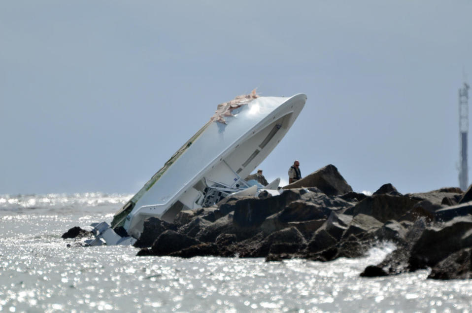 Investigators look at a boat overturned on a jetty