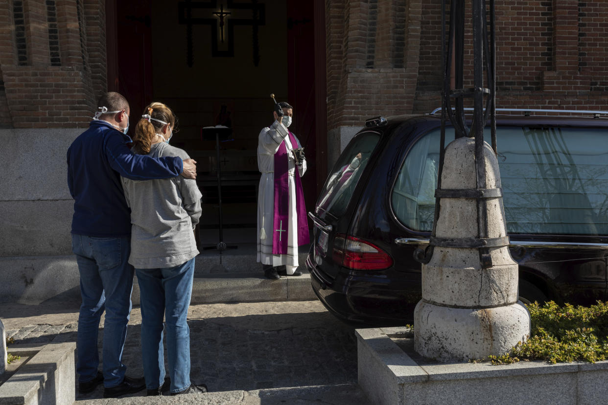 A priest wearing a face masks to protect against coronavirus performs funeral rites at a Madrid cemetery during the coronavirus outbreak in Madrid, Spain, Friday, March 27, 2020. The new coronavirus causes mild or moderate symptoms for most people, but for some, especially older adults and people with existing health problems, it can cause more severe illness or death. (AP Photo/Bernat Armangue)