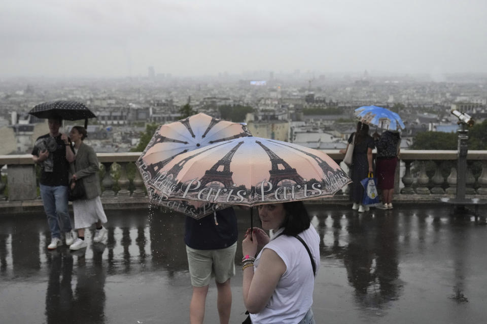 Personas en el distrito de Montmarte sacar los paraguas debido a que la lluvia amenaza a París durante la ceremonia de apertura de los Juegos Olímpicos el viernes 26 de julio del 2024. (AP Foto/Dita Alangkara)