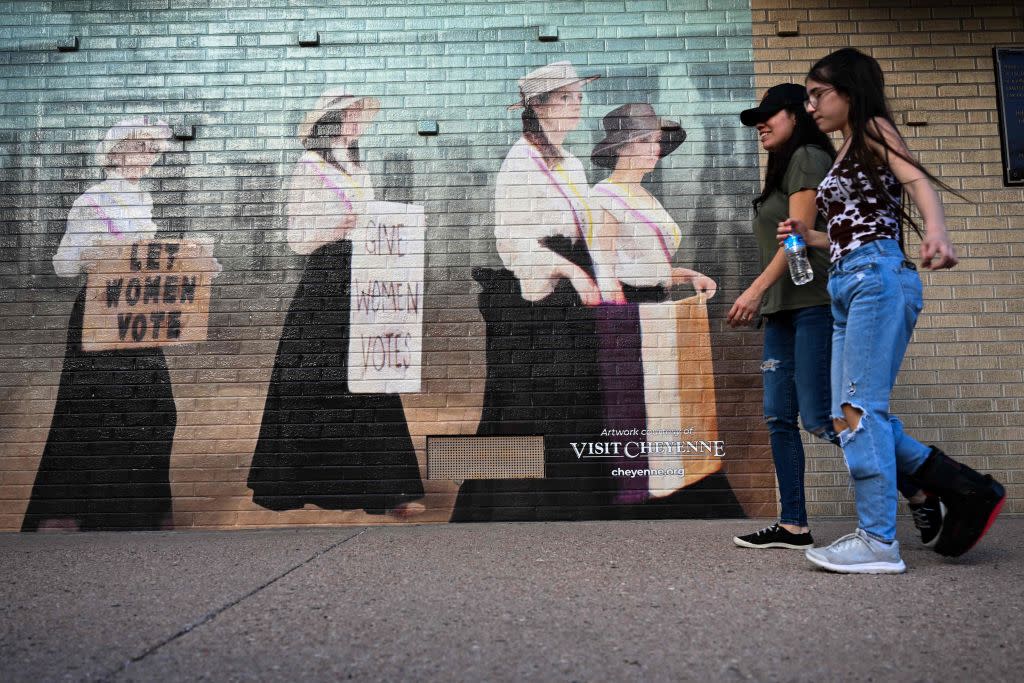 People walk past a mural of featuring a representation of women seeking the right to vote,