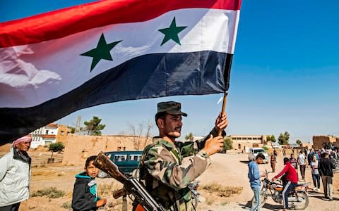 A Syrian regime soldier waves the national flag a street on the western entrance of the town of Tal Tamr in the countryside of Syria's northeastern Hasakeh province on October 14, 2019 - Credit: AFP