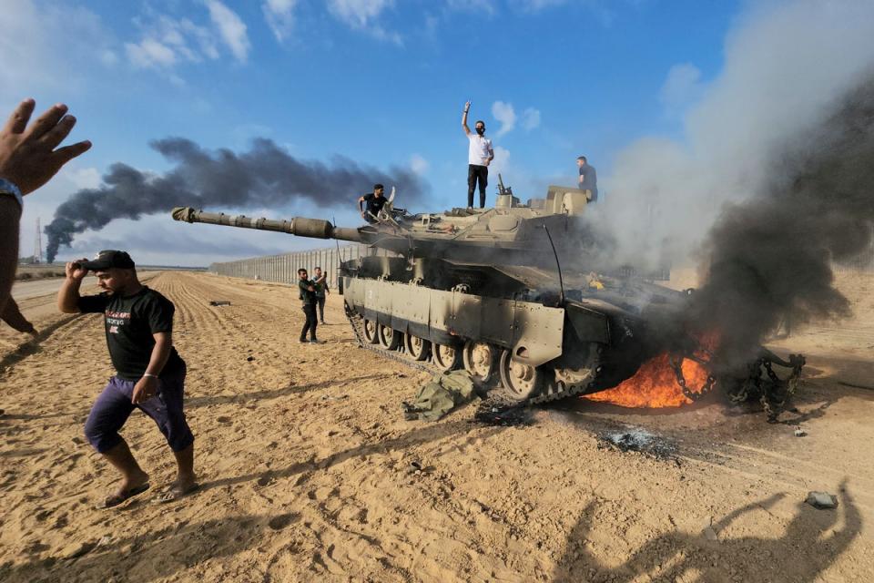 Hamas militants next to a destroyed Israeli tank at the Gaza Strip fence east of Khan Younis (AP)