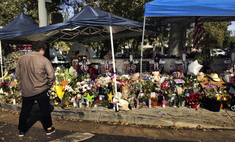 FILE— A passerby stops to look over a street side memorial to the shooting victims of the Borderline Bar in Thousand Oaks, Calif., on Tuesday, Nov. 27, 2018. Video released from body cameras worn by deputies who responded to the mass shooting captures the chaos deputies encountered when they arrived at the scene. The video was released Tuesday, Jan. 18., 2022, after a court fight by the Associated Press and other news outlets to have the it released. (AP Photo/Amanda Lee Myers, File)