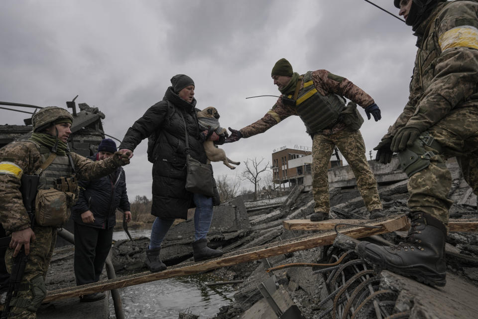 Ukrainian servicemen help a woman carrying a small dog across the Irpin River on an improvised path while assisting people fleeing the town of Irpin, Ukraine, Saturday, March 5, 2022. (AP Photo/Vadim Ghirda)