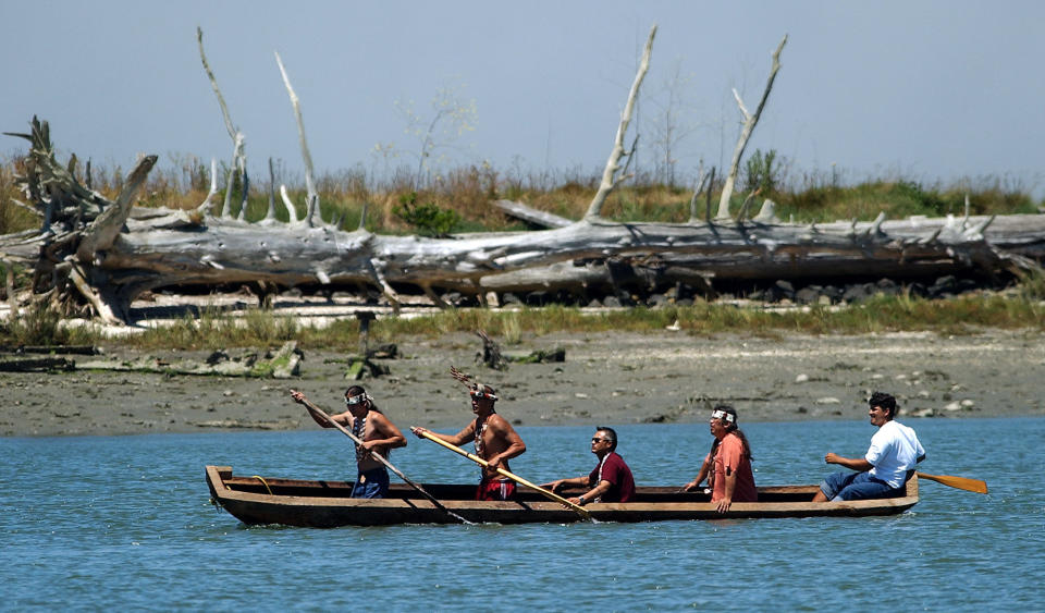 FILE - Indians of the Wiyot Tribe paddle a dugout redwood canoe from Indian Island, background, across Humboldt Bay Friday, June 25, 2004, in Eureka, Calif. The remains of 20 Native Americans massacred in the 1860s on the Northern California island have been returned to their tribe from a museum where they had been in storage. The tribe's historic preservation officer says the remains will be reunited with their families. (AP Photo/Ben Margot,File)