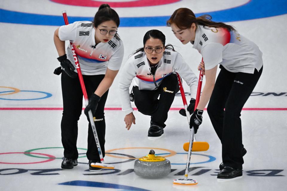 South Korea's Kim Eun-jung (C) curls the stone as teammates Kim Cho-hi (R) and Kim Seon-yeoung (L) prepares to sweep (AFP via Getty Images)