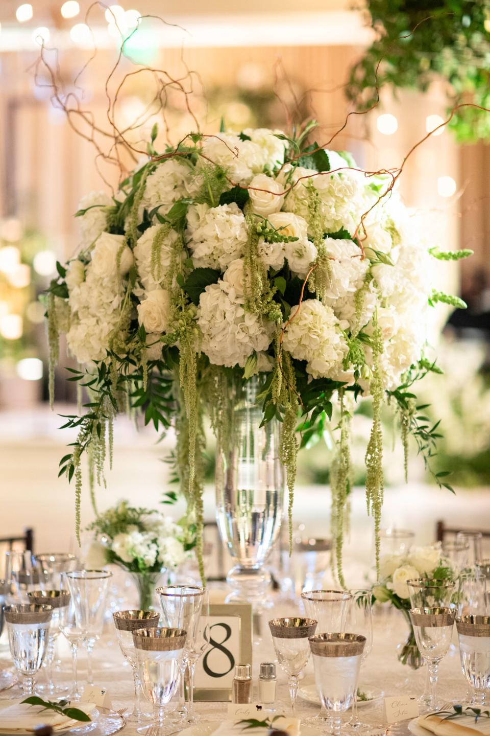 Trumpet vases with all white hydrangeas, lisianthus, roses, orchids, double blooming peonies, and more with amaranthus trailing down.