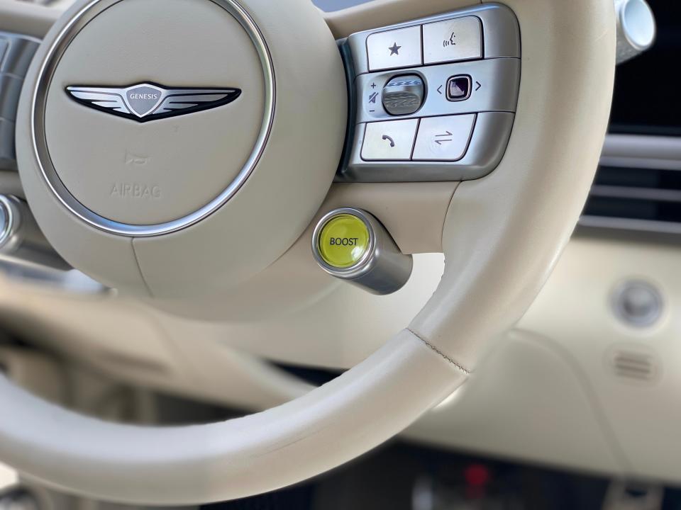 The yellow boost button on the lower right corner of a Genesis GV60 EV's creme-colored steering wheel.