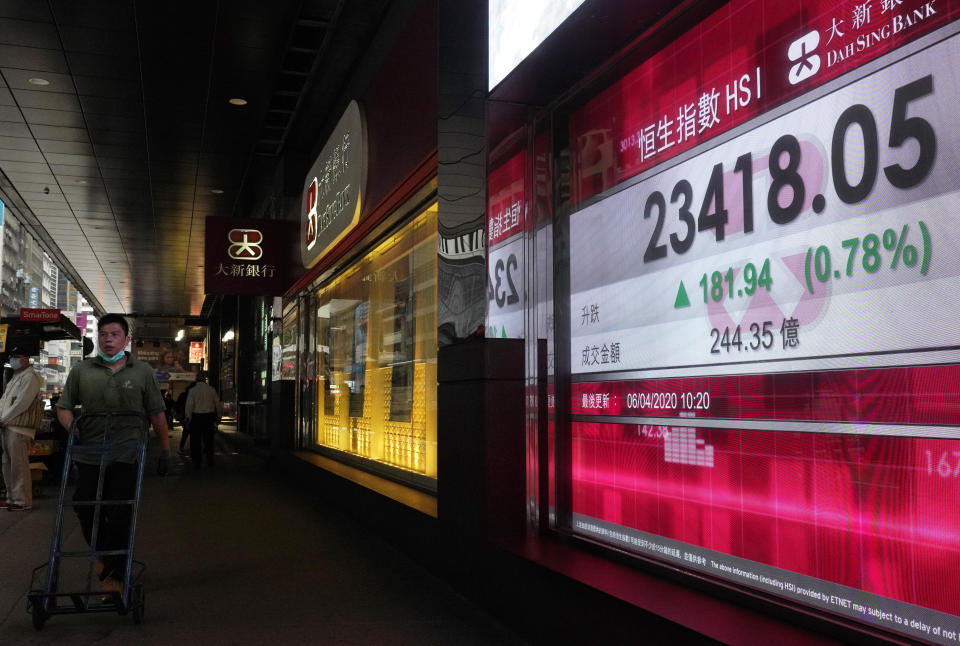 A man wearing face mask walks past a bank electronic board showing the Hong Kong share index at Hong Kong Stock Exchange Monday, April 6, 2020. Asian shares and U.S. futures have rebounded as investors grasped at threads of hope that the battle against the coronavirus pandemic may be making some progress in some hard-hit areas.(AP Photo/Vincent Yu)