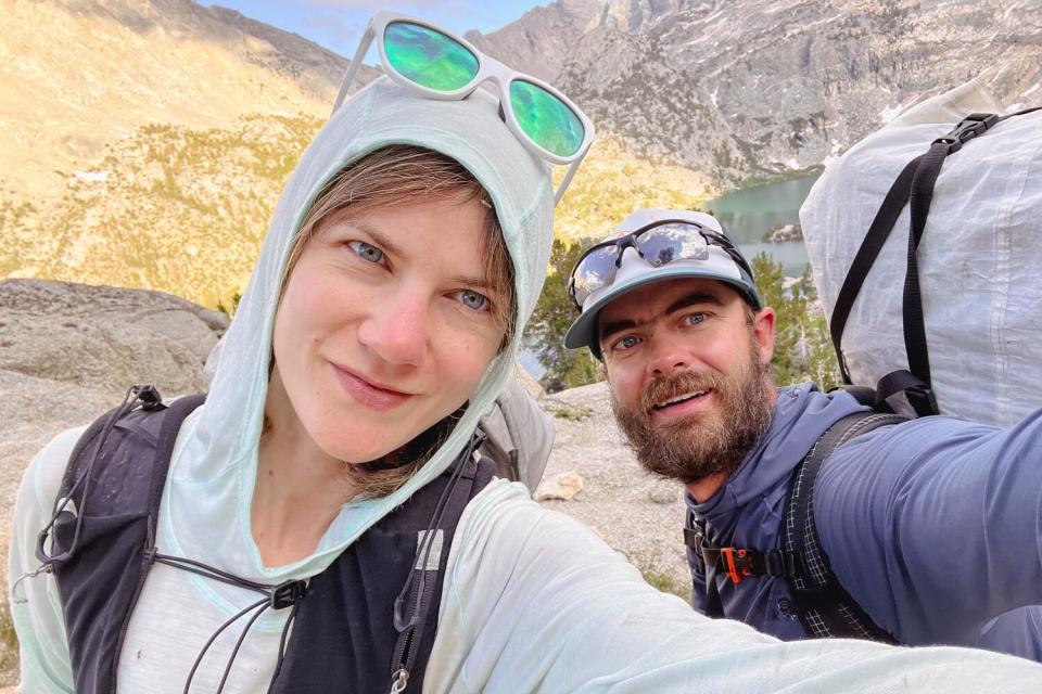 A woman and man take a selfie with mountains in the background.