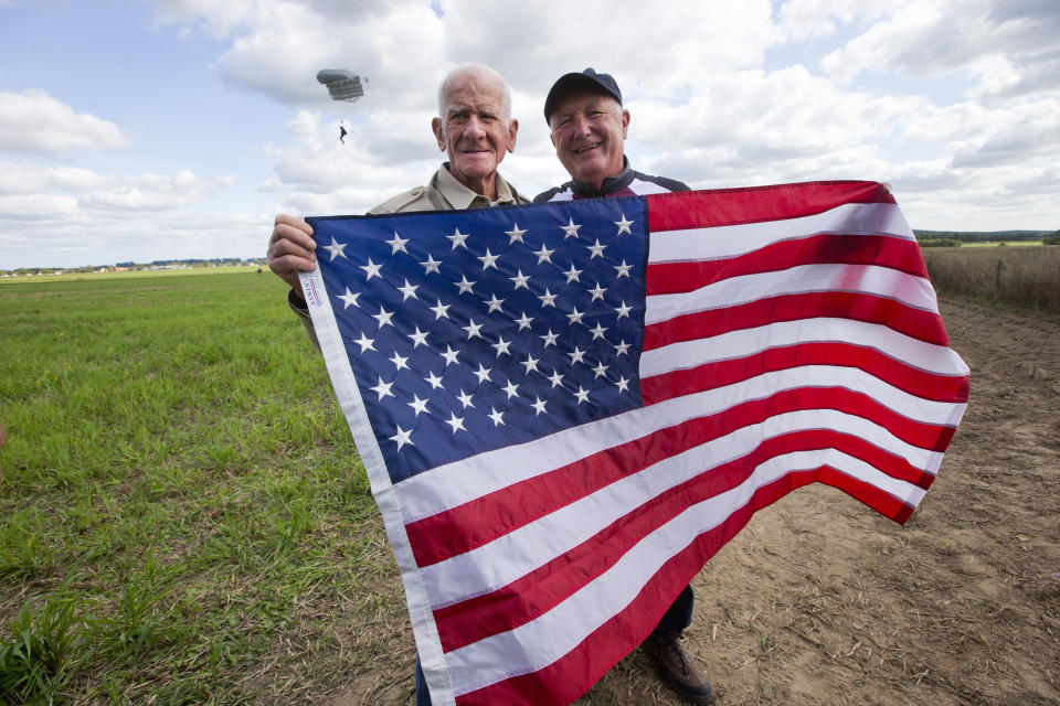 Tom Rice, a 98-year-old American WWII veteran, and U.S. Ambassador Pete Hoekstra, right, pose with the U.S. flag after landing with a tandem parachute jump from a plane near Groesbeek, Netherlands, Thursday, Sept. 19, 2019, as part of commemorations marking the 75th anniversary of Operation Market Garden. Rice jumped with the U.S. Army's 101st Airborne Division in Normandy, landing safely despite catching himself on the exit and a bullet striking his parachute. (AP Photo/Peter Dejong)