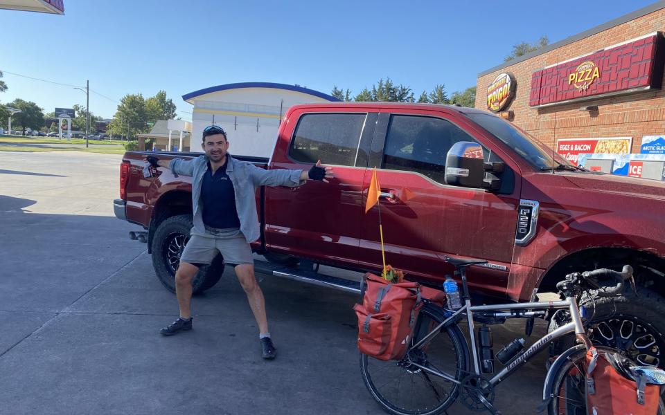 The author stands with his bicycle in front of a large pick-up truck