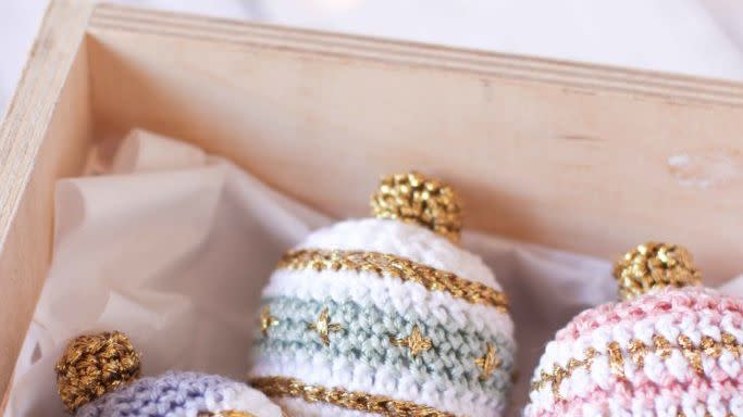 small and larger crocheted christmas bauble ornaments in pastel colors including pink, lavender and green on tissue paper in a box