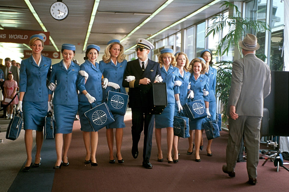 Leonardo Di Caprio walks through an airport with a whole group of flight attendants on his arm