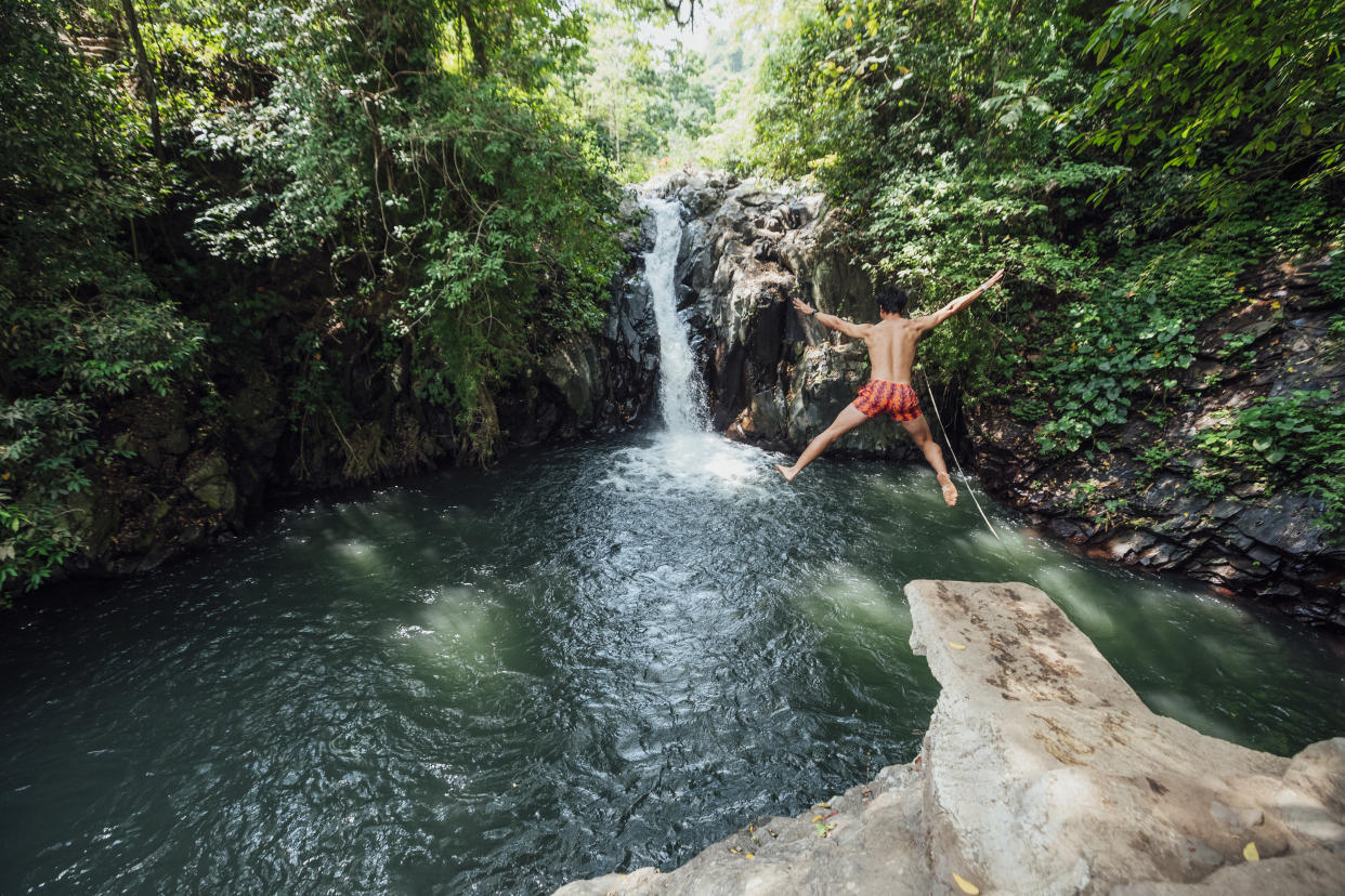 A young man jumping off a cliff edge next to the waterfalls in the idyllic destination of Bali. (Photo: Getty)