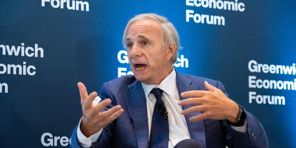 Bridgewater founder Ray Dalio gestures in front of a blue and white background.