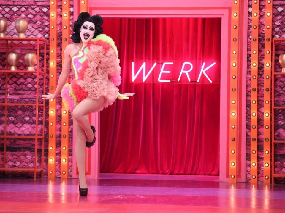 Gottmik in a red and yellow look and black wig on the set of drag race