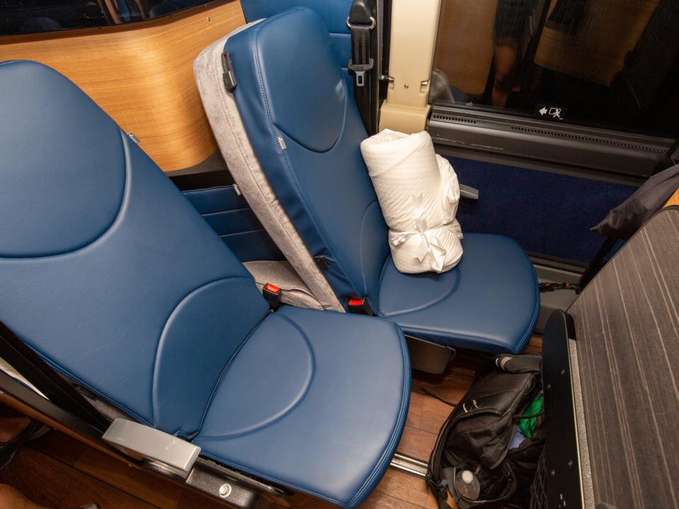 Two staggered bus seats with a pillow on one of the seats.