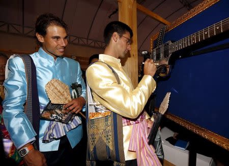 Tennis player Rafael Nadal (L) of Spain looks on as Novak Djokovic (R) of Serbia signs his autograph on a guitar during a visit to a fair after meeting with Thai Prime Minister Prayut Chan-o-cha (not pictured) at a market outside Government House in Bangkok, Thailand, October 2, 2015. REUTERS/Rungroj Yongrit/Pool