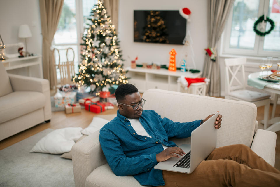 Handsome African American male student sitting at home, working using his laptop during winter holidays