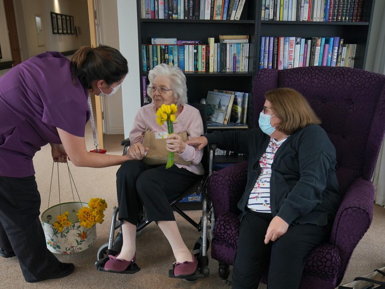 A member of staff gives a bunch of daffodils to Sylvia Newsom (centre) and her daughter Kay Fossett (right), who haven't seen each other since December, enjoy their first visit following the easing of rules at Gracewell of Sutton care home in South London (Aaron Chown/PA)