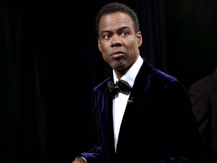 An image of Chris Rock wearing a tuxedo, carrying a red envelope