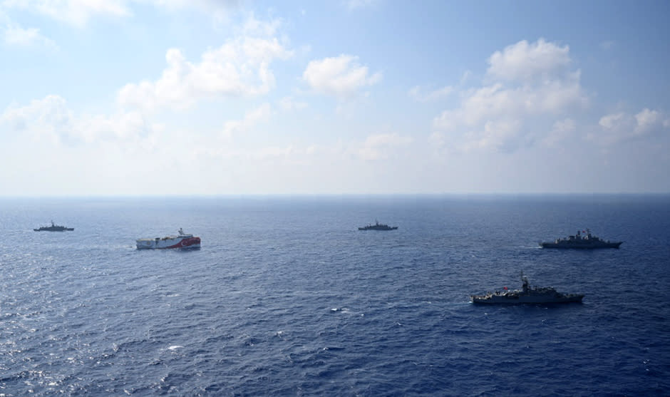 In this photo provided by the Turkish Defense Ministry, Turkey's research vessel, Oruc Reis, in red and white, is surrounded by Turkish navy vessels as it was heading in the west of Antalya on the Mediterranean, Turkey, Monday, Aug 10, 2020. Tension remains high between Greece and Turkey, whose warships are in the eastern Mediterranean where Turkey has sent a research vessel to carry out seismic research for energy resources in an area Greece says is on its continental shelf.(Turkish Defense Ministry via AP, Pool)