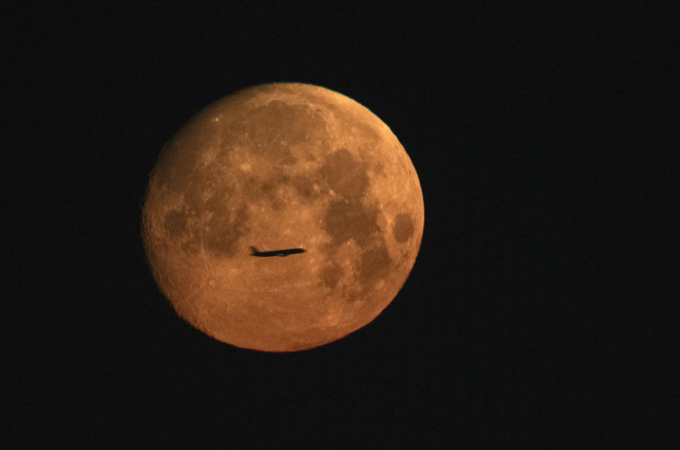 The silhouette of a plane can be seen in front of the full moon