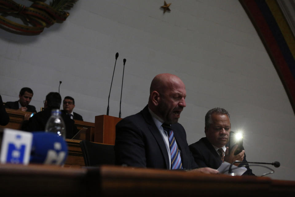 A lawmaker uses his cell phone for light after the lights went out at the National Assembly in Caracas, Venezuela, Tuesday, Jan. 7, 2020. Lawmakers continued in the dimly lit assembly, shouting into microphones that did not work to declare opposition leader Juan Guaidó the legitimate president of the congress. (AP Photo/Andrea Hernandez Briceño)