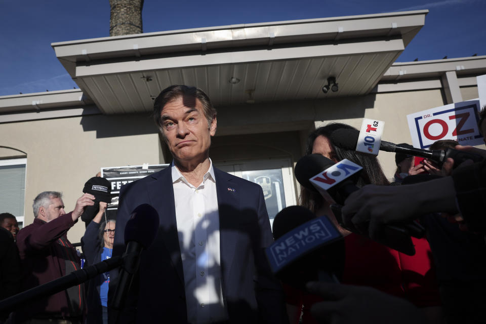 Dr. Mehmet Oz at a polling station wearing a dubious expression, as reporters point their microphones at him.