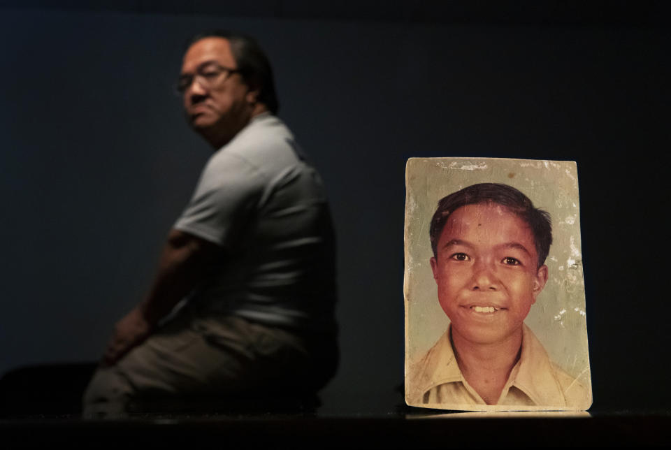 A sexual abuse survivor who would only go by the initials C.M.V., 58, sits behind a photo of himself when he was about 11 years old, in Hagatna, Guam, Saturday, May 11, 2019. C.M.V. says in a lawsuit he was sexually molested between the ages of 9 and 13 by Monsignor Jose Ada Leon Guerrero, a priest at the time at Nino Perdido y Sagrada Familia Catholic Church where C.M.V. served as an altar boy. "I try not to think about it," said C.M.V. about his abuse before becoming too overcome with emotion to continue talking about it. Guerrero is now dead. (AP Photo/David Goldman)