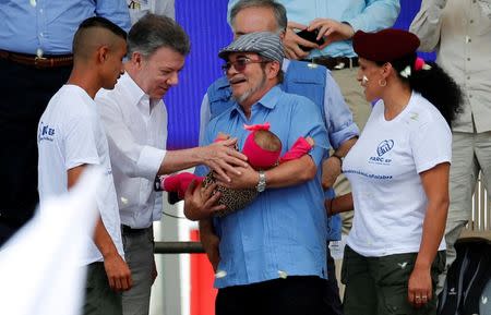 Colombia's Marxist FARC rebel leader Rodrigo Londono, also known as Timochenko, holds a baby next to Colombian president Juan Manuel Santos as they attend the final act of abandonment of arms in Mesetas, Colombia June 27, 2017. REUTERS/Jaime Saldarriaga