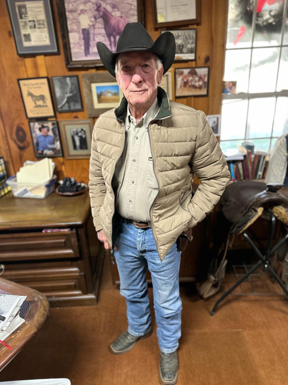 Bobby Melton stands in front of the wall of his office covered in autographed photos, his grandfather's horse selling license from 1920, and photos of him and his family showing their Quarter horses