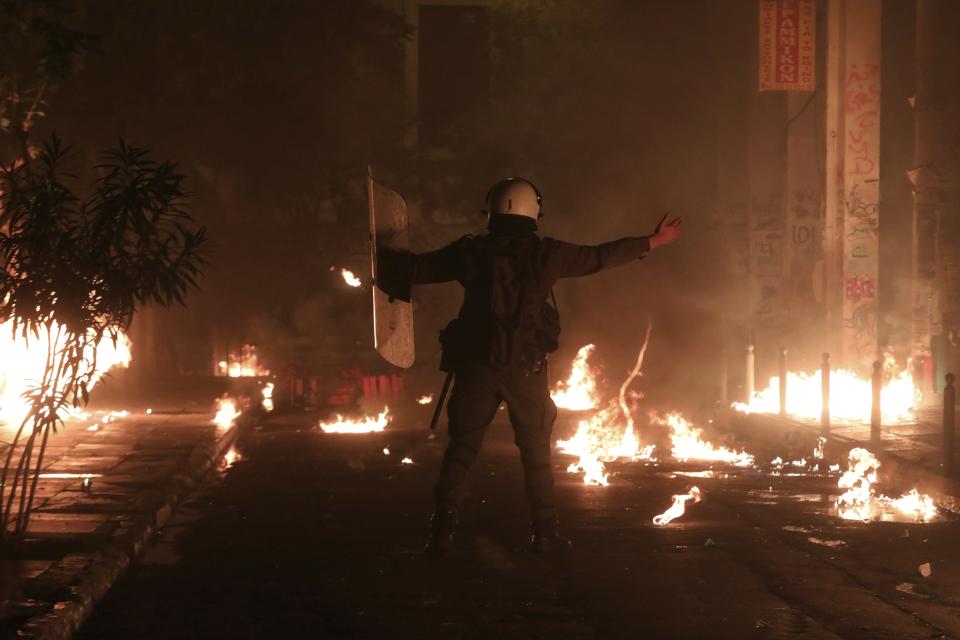 A riot policeman raises his hands up as hooded youths throw petrol bombs during clashes in the Athens neighborhood of Exarchia, a haven for extreme leftists and anarchists, Saturday, Nov. 17, 2018. Clashes have broken out between police and anarchists in central Athens on the 45th anniversary of a student uprising against Greece's then-ruling military regime. (AP Photo/Yorgos Karahalis)