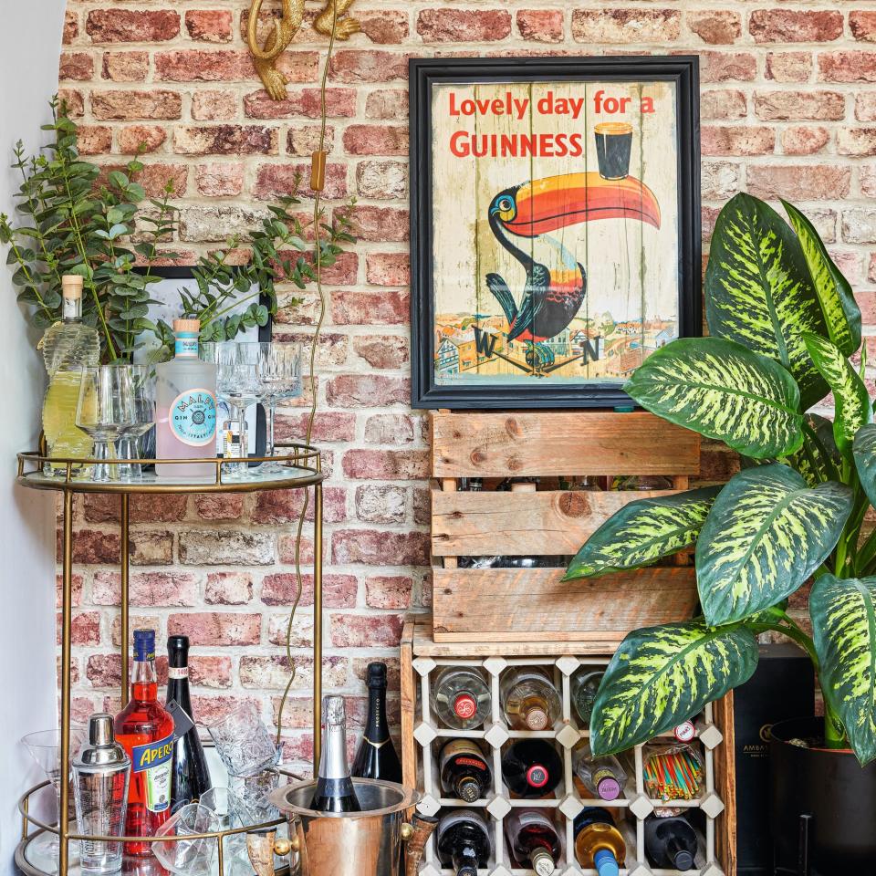  Exposed brick wall behind drinks counter with plants and framed art. 