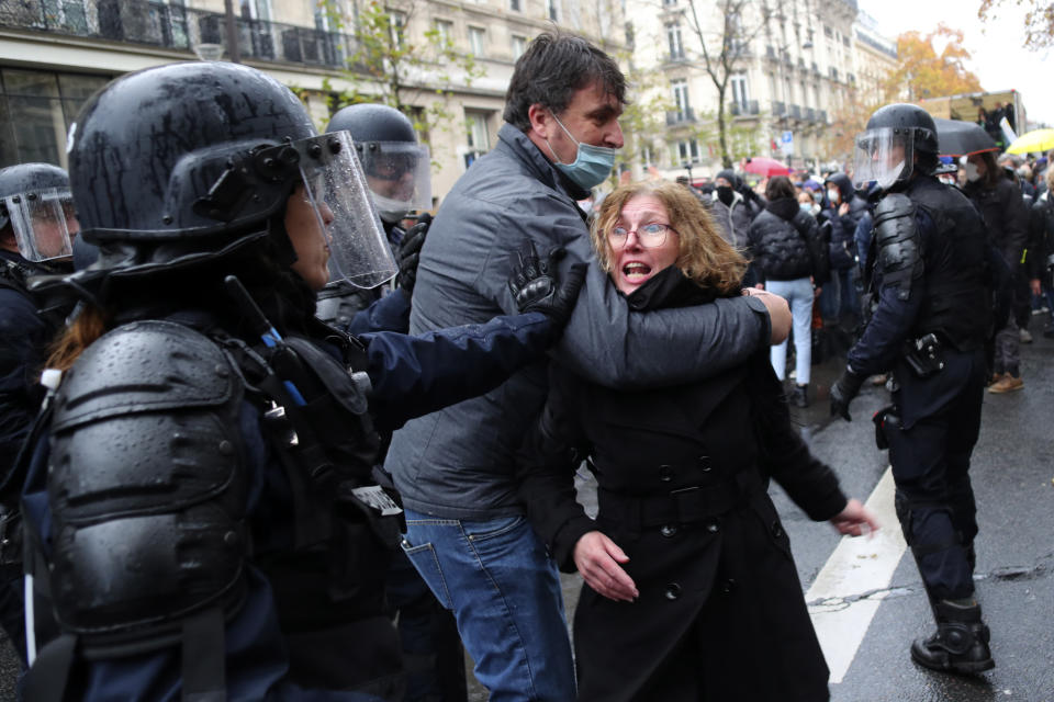 A riot police officer pushes a couple during a protest, Saturday, Dec.12, 2020 in Paris. Protests are planned in France against a proposed bill that could make it more difficult for witnesses to film police officers. (AP Photo/Thibault Camus)