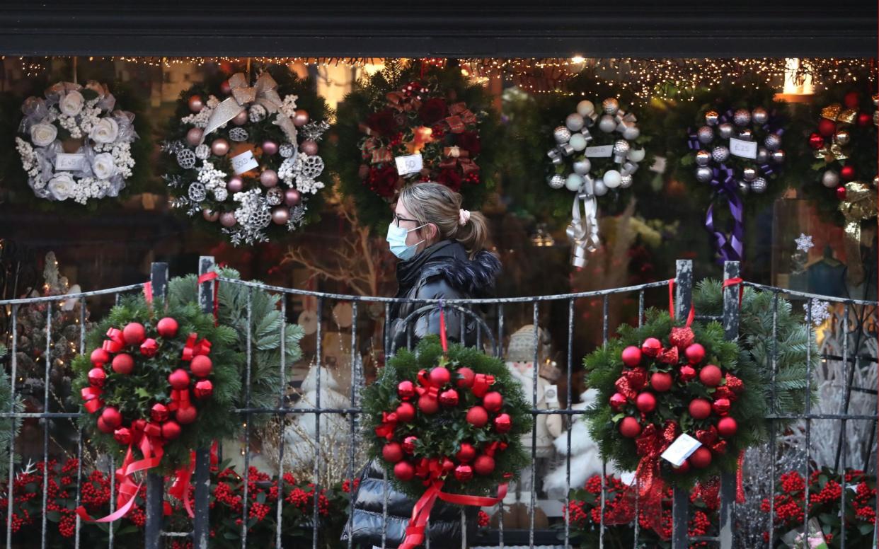 A person wearing a face covering walks past a display of Christmas wreaths -  Andrew Milligan/PA