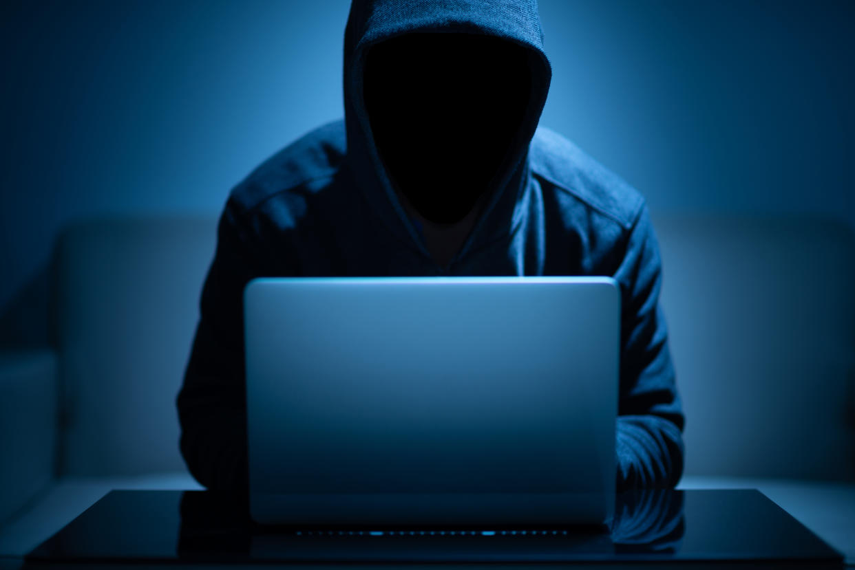 Hooded man using laptop in the dark room