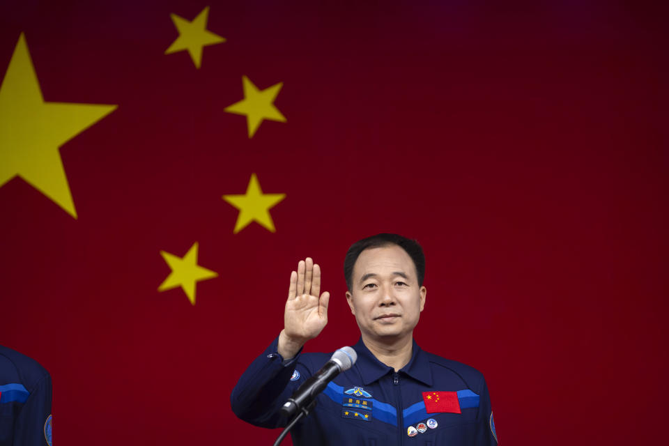 Jing Haipeng, a Chinese astronaut for the upcoming Shenzhou-16 mission, waves behind glass during a meeting of the press at the Jiuquan Satellite Launch Center in northwest China on Monday, May 29, 2023. China's space program plans to land astronauts on the moon before 2030, a top official with the country's space program said Monday. (AP Photo/Mark Schiefelbein)
