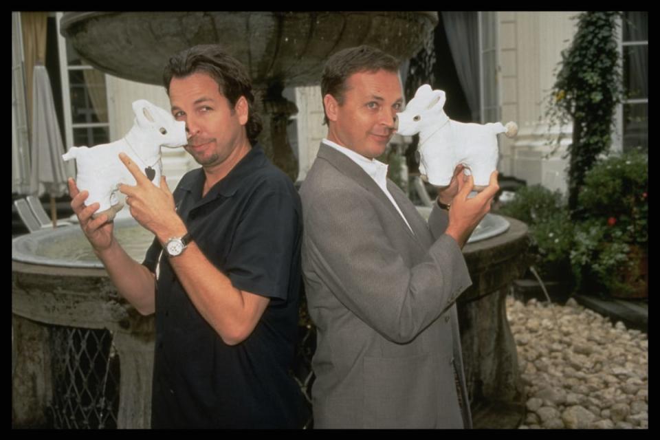 Peter and Bobby Farrelly stand back to back with prop dogs in full body casts in their hands